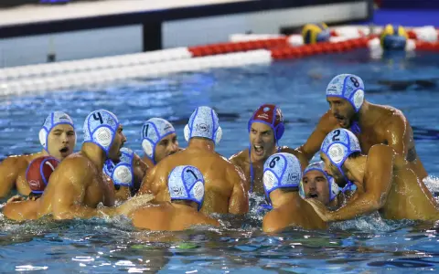 Giocatori di pallanuoto in acqua, con cuffie numerate, in un momento di intensa competizione. I loro ruoli pallanuoto sono evidenti dalla loro posizione e dall'azione.