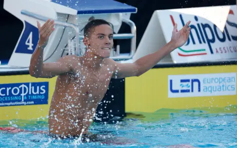 David Popovici esulta in piscina, circondato da schizzi d'acqua, con il numero 4 sulla corsia.