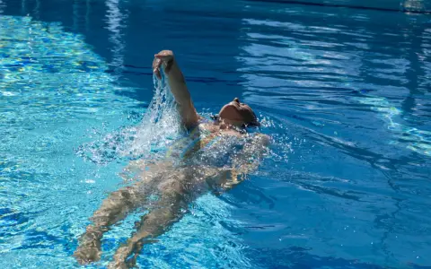 Donna nuota a dorso in una piscina olimpionica, godendosi la profondità e la frescura dell'acqua cristallina.