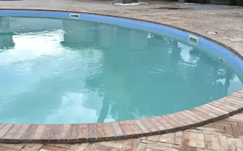 Piscina con acqua torbida e riflessi del cielo, circondata da un bordo in mattoni.