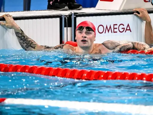 Adam Peaty, con cuffia rossa e occhialini, emerge dall'acqua della piscina, aggrappato al bordo.