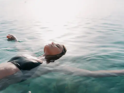Donna galleggia sull'acqua, superando la paura di nuotare dove non si tocca. La luce del sole illumina il suo viso sereno.