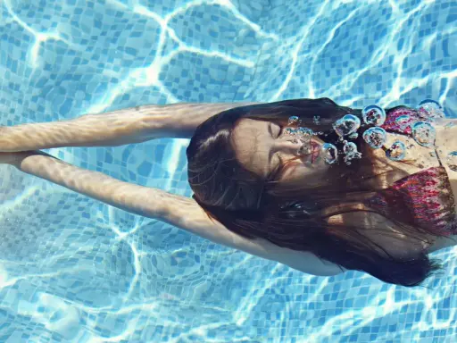 Ragazza nuota sott'acqua, capelli scuri fluttuano. Le bollicine d'aria evidenziano gli effetti del cloro sui capelli.