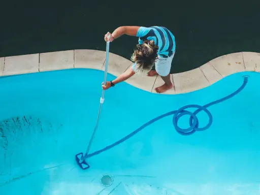 Ragazzo pulisce la piscina con un aspirafango piscina fai da te, rimuovendo detriti dal fondo azzurro.