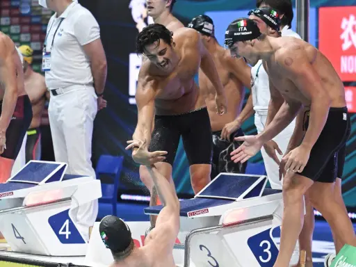 Atleti italiani festeggiano dopo la staffetta 4x100. Un nuotatore porge la mano a un compagno, gioia e sudore bagnano la corsia.
