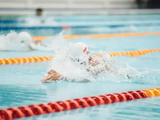 Nuotatore in azione, concentrato su come nuotare più veloce. Schizzi d'acqua e bracciate potenti in piscina.