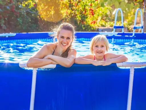 Donna e bambina sorridono in piscina. L'acqua limpida, forse trattata con bicarbonato, riflette il sole.