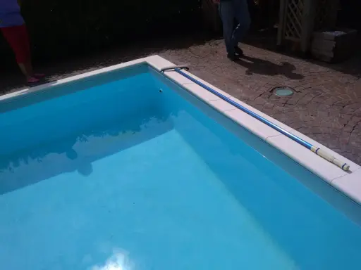 Piscina bucata: un'asta telescopica blu giace sul bordo bianco, pronta per cercare il buco.