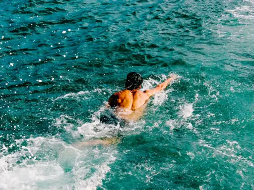 Uomo con schiena muscolosa nuotare in mare aperto, circondato da spruzzi d'acqua cristallina.