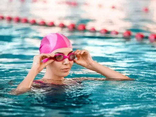 Donna con cuffia e occhialini rosa in piscina, pronta a godere dei benefici piscina.