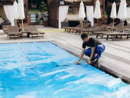 Uomo in blu sistema il telo in pvc della piscina, un passo fondamentale per capire come pulire il telo in pvc della piscina e mantenerla splendente.