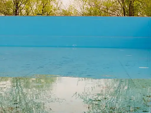 La piscina in inverno va svuotata. L'acqua residua riflette il verde degli alberi e il cielo, mentre il fondo mostra i segni del tempo.