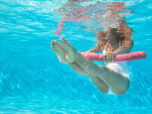 Donna esegue esercizi gambe piscina con un galleggiante rosa.