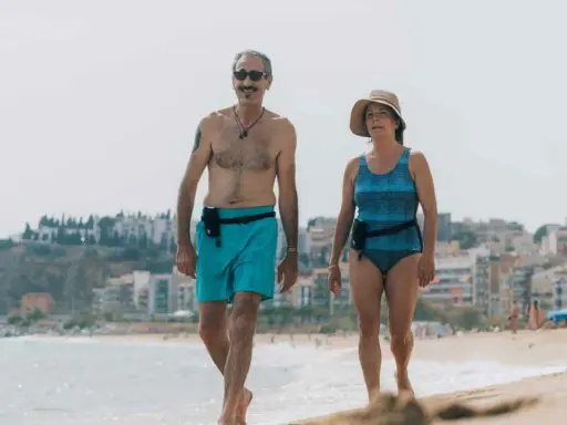 Coppia over 60 passeggia sulla spiaggia, un esempio di allenamento nuoto e vita attiva.