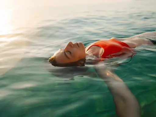 Donna galleggia serena in acqua cristallina, pensando ai rimedi per l'otite del nuotatore.