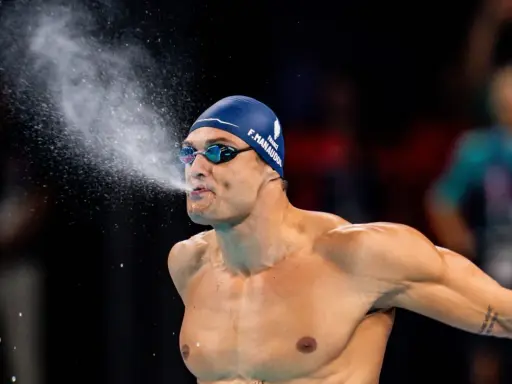 Florent Manaudou, nuotatore francese, spruzza acqua dalla bocca dopo una gara, con la cuffia blu e gli occhialini da nuoto.
