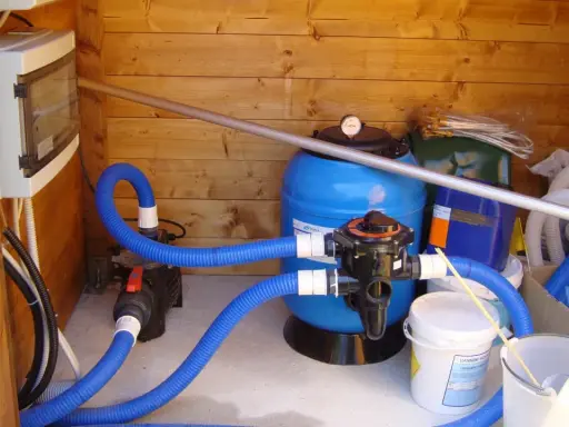Sistema di filtrazione per piscina con filtro a sabbia, pompa e tubi blu. Il filtro a sabbia è il cuore del sistema per mantenere l'acqua pulita.