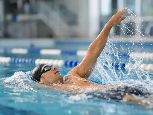 Atleta in piscina esegue la nuotata a **scheda dorso**, con il braccio destro sollevato e l'acqua che schizza.