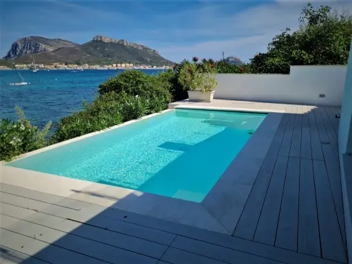 Piscina cristallina con vista mare. L'acqua, mantenuta con candeggina a un ph ideale, riflette il cielo azzurro e le montagne sullo sfondo.
