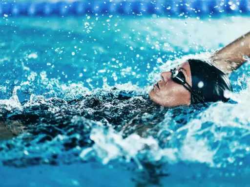 Atleta in nuoto dorso, godendo dei benefici di questo sport. L'acqua schizza intorno al suo viso concentrato.