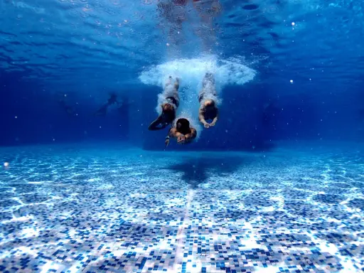 Subacquea, tre persone si tuffano in piscina. Chissà in quanto tempo un adulto impara a nuotare, ma loro sembrano già a loro agio.
