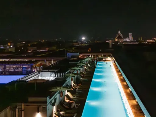 Una splendida piscina di sera, illuminata da luci soffuse, con la silhouette di Firenze sullo sfondo.