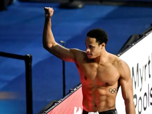 Shane Tusup, nuotatore con un pugno alzato, celebra una vittoria. Sul suo petto, i cinque cerchi olimpici.