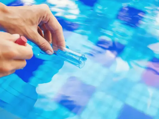Mano che preleva campione d'acqua piscina con provetta. Il cloro basso indica necessità di trattamento.