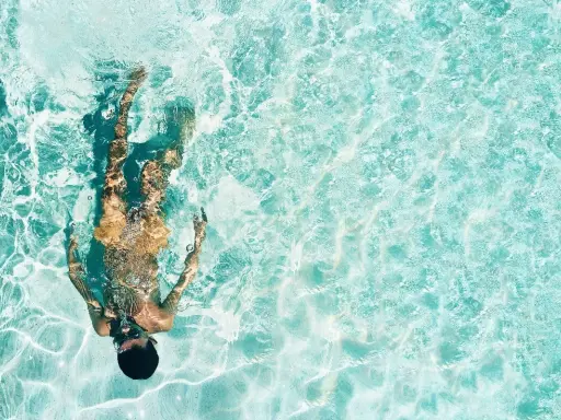 Persona sott'acqua in piscina, con riflessi luminosi. Chissà se il suo tatuaggio è fresco, dopo quanto tempo in piscina?