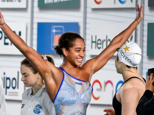 Atleta festeggia vittoria nel nuoto, braccia alzate con gioia.