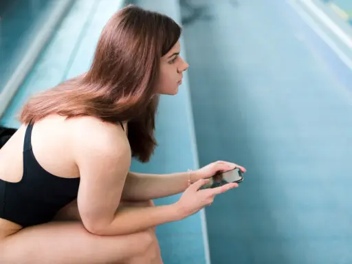 Ragazza in costume da bagno nero, con cellulare in mano, pronta a perdere 10 kg con il nuoto.