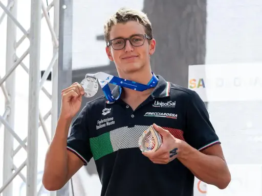 Davide Grossi, nuotatore italiano, mostra con orgoglio le sue medaglie d'argento e di bronzo, frutto di un'ottima prestazione.