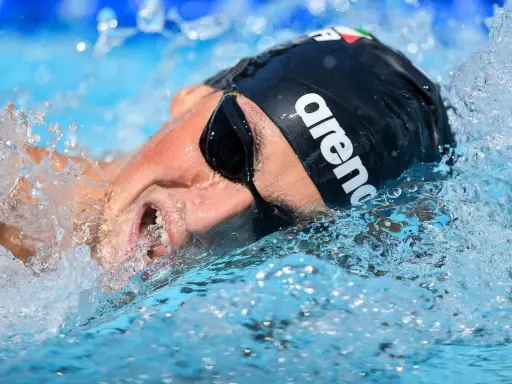 Nuotatore con cuffia Arena e occhialini, immerso nell'acqua con spruzzi. Potrebbe essere Pasquale Giordano in azione.