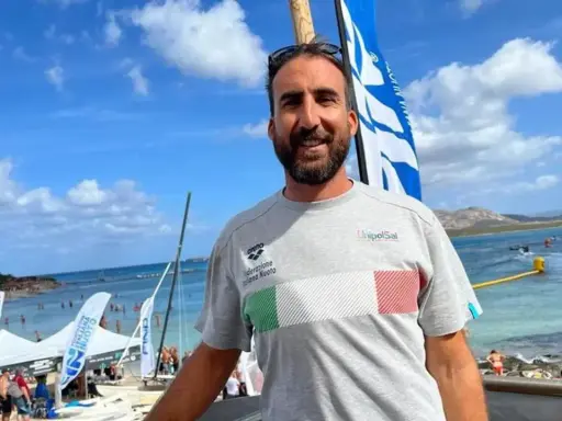 Fabrizio Antonelli sorride in spiaggia, con la bandiera italiana sul petto, pronto per un evento di nuoto.