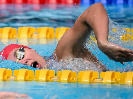 Nuotatrice con cuffia rossa e occhialini, in azione in piscina. Camille Muffat, un'atleta determinata.