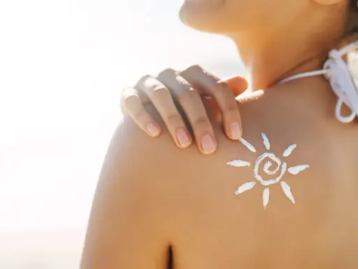Sole sulla pelle, ma attenzione: il cloro toglie l'abbronzatura. Crema solare a forma di sole sulla spalla di una donna in spiaggia.