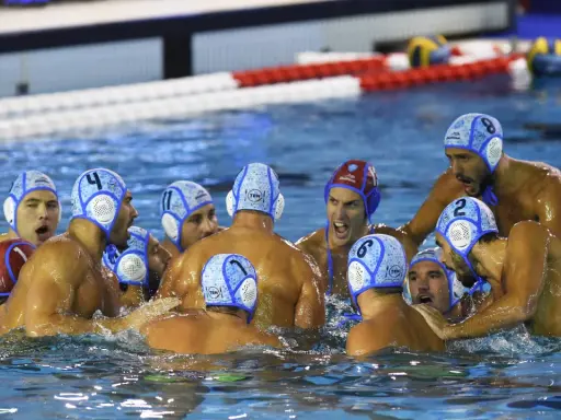 Giocatori di pallanuoto in acqua, con cuffie numerate, in un momento di intensa competizione. I loro ruoli pallanuoto sono evidenti dalla loro posizione e dall'azione.
