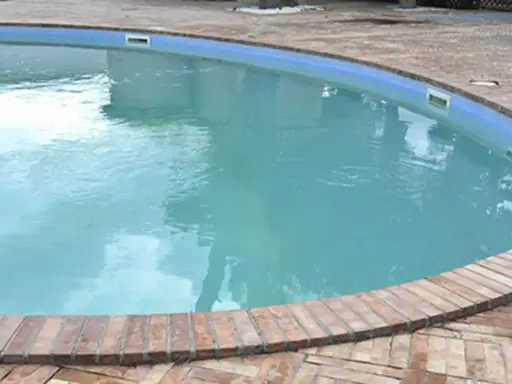 Piscina con acqua torbida e riflessi del cielo, circondata da un bordo in mattoni.