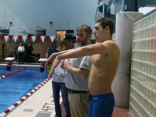 Nuotatore pronto a gareggiare, forse Matt Grevers, con allenatori al bordo piscina.