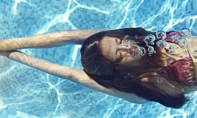 Ragazza nuota sott'acqua, capelli scuri fluttuano. Le bollicine d'aria evidenziano gli effetti del cloro sui capelli.