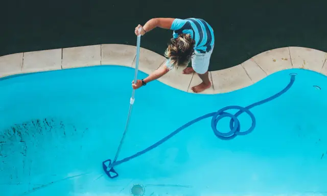 Ragazzo pulisce la piscina con un aspirafango piscina fai da te, rimuovendo detriti dal fondo azzurro.