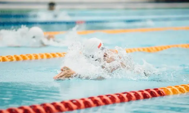 Nuotatore in azione, concentrato su come nuotare più veloce. Schizzi d'acqua e bracciate potenti in piscina.