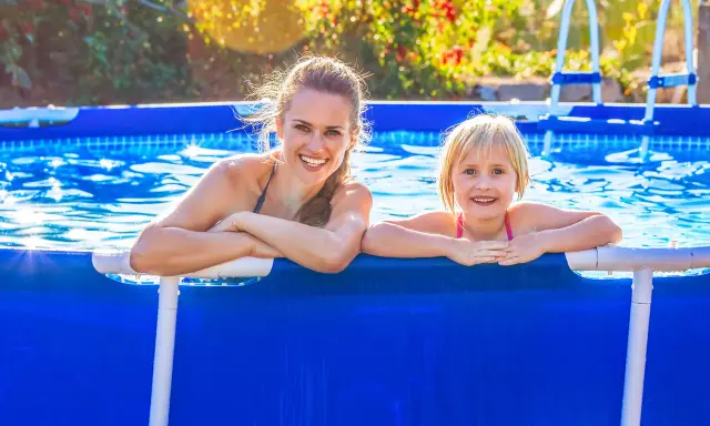 Donna e bambina sorridono in piscina. L'acqua limpida, forse trattata con bicarbonato, riflette il sole.
