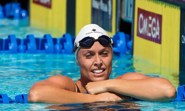 Amanda Beard, nuotatrice sorridente in piscina, con cuffia e occhialini, pronta per la gara.