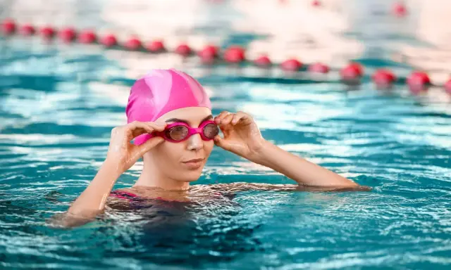 Donna con cuffia e occhialini rosa in piscina, pronta a godere dei benefici piscina.