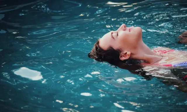 Donna galleggia serena, un passo verso come vincere la paura dell'acqua da adulti. L'acqua turchese la culla, simbolo di pace ritrovata.