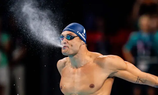 Florent Manaudou, nuotatore francese, spruzza acqua dalla bocca dopo una gara, con la cuffia blu e gli occhialini da nuoto.