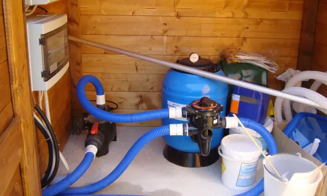 Sistema di filtrazione per piscina con filtro a sabbia, pompa e tubi blu. Il filtro a sabbia è il cuore del sistema per mantenere l'acqua pulita.