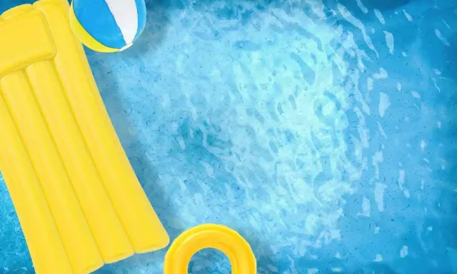 Un materassino giallo, una palla e un salvagente galleggiano in una piscina azzurra. Ideale per scoprire come pulire piscina gonfiabile.