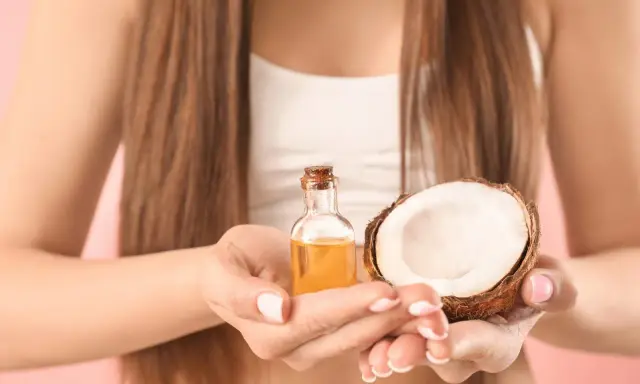 Mani che tengono una boccetta di olio di cocco e mezzo cocco. Ideale per proteggere i capelli dopo la piscina.